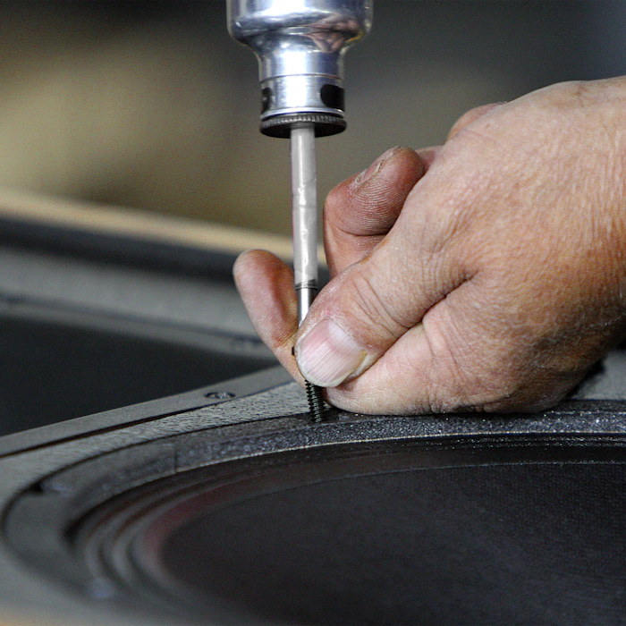 A Klipsch Craftsman hand fastening a speaker to its cabinet mobile