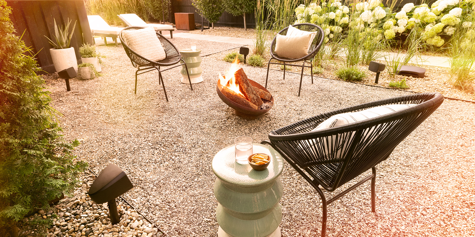 Klipsch Courtyard Speakers outside on cozy patio with fire pit at golden hour 2000x1000