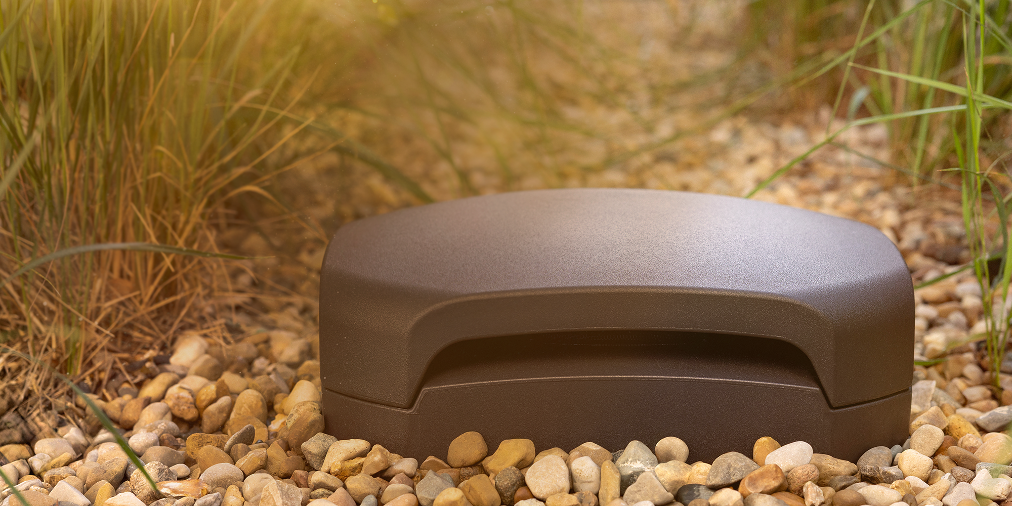 Klipsch Courtyard Subwoofer outside buried in patio gravel at golden hour 3 2000x1000