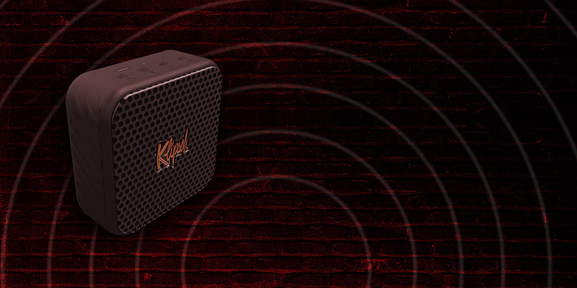Klipsch Daredevil Partnership Klipsch Austin portable speaker against dark red brick wall with circles emanating 2000x1000