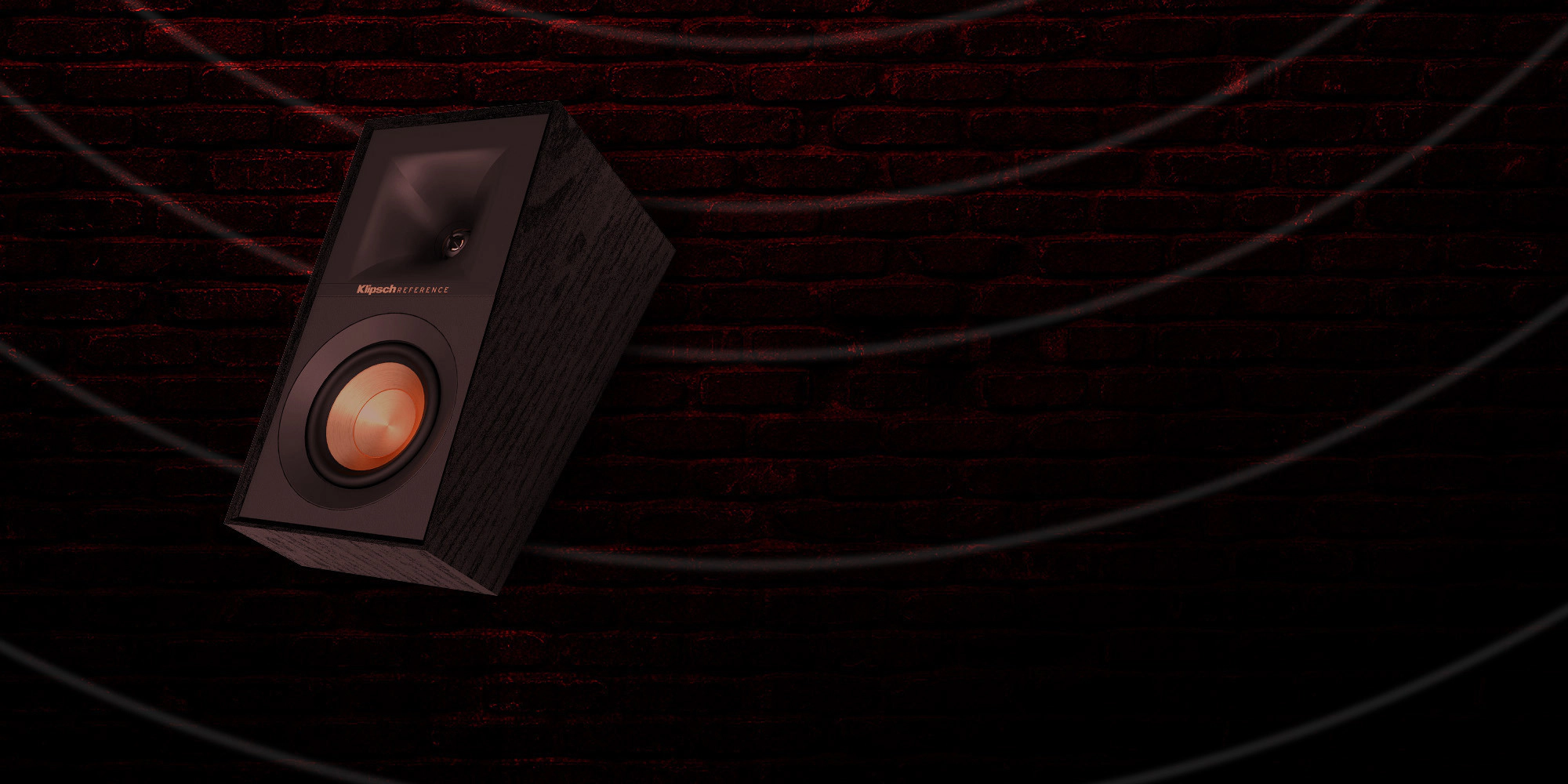 Klipsch Daredevil Partnership Klipsch Reference surround speaker against dark red brick wall with circles emanating 2000x1000
