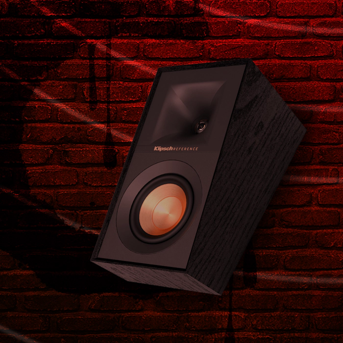 Klipsch Daredevil Partnership Klipsch Reference surround speaker against dark red brick wall with circles emanating 2000x2000