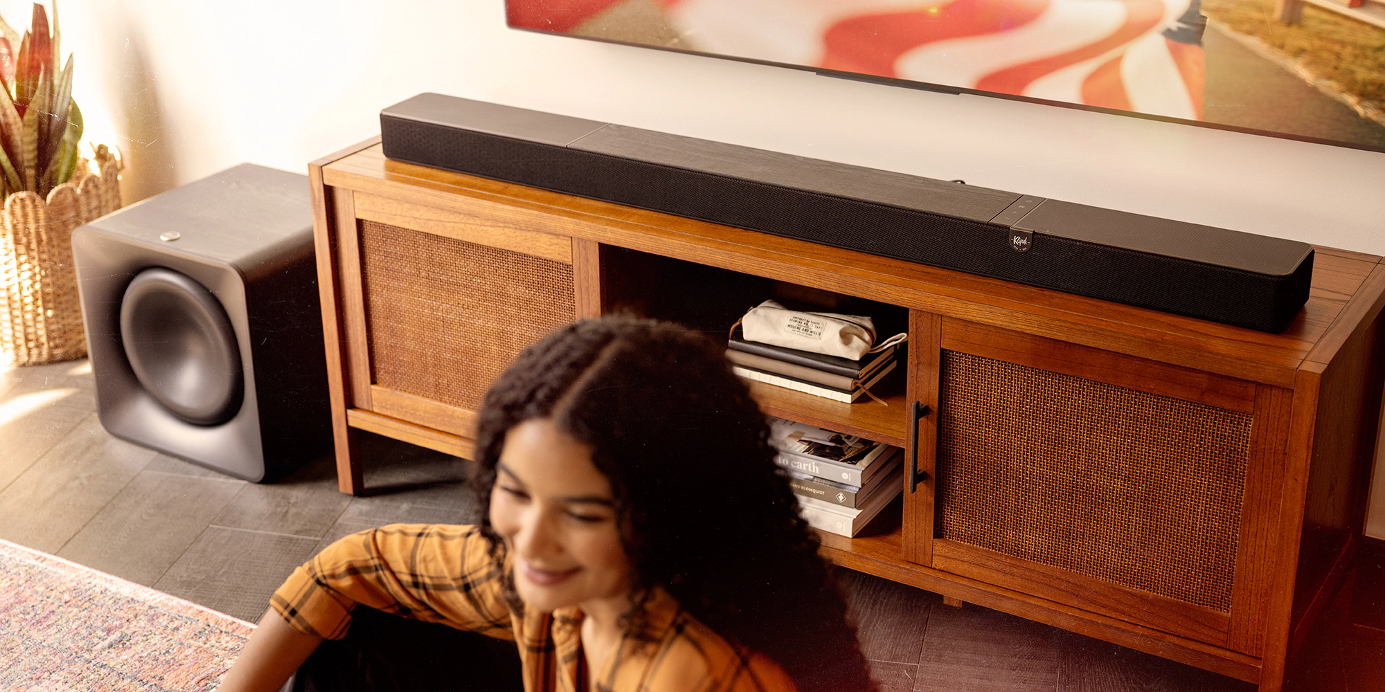 Klipsch Flexus CORE 300 BK and SUB 200 in focus in sunny living room with American flag on tv and woman in blurred foreground 2000x1000