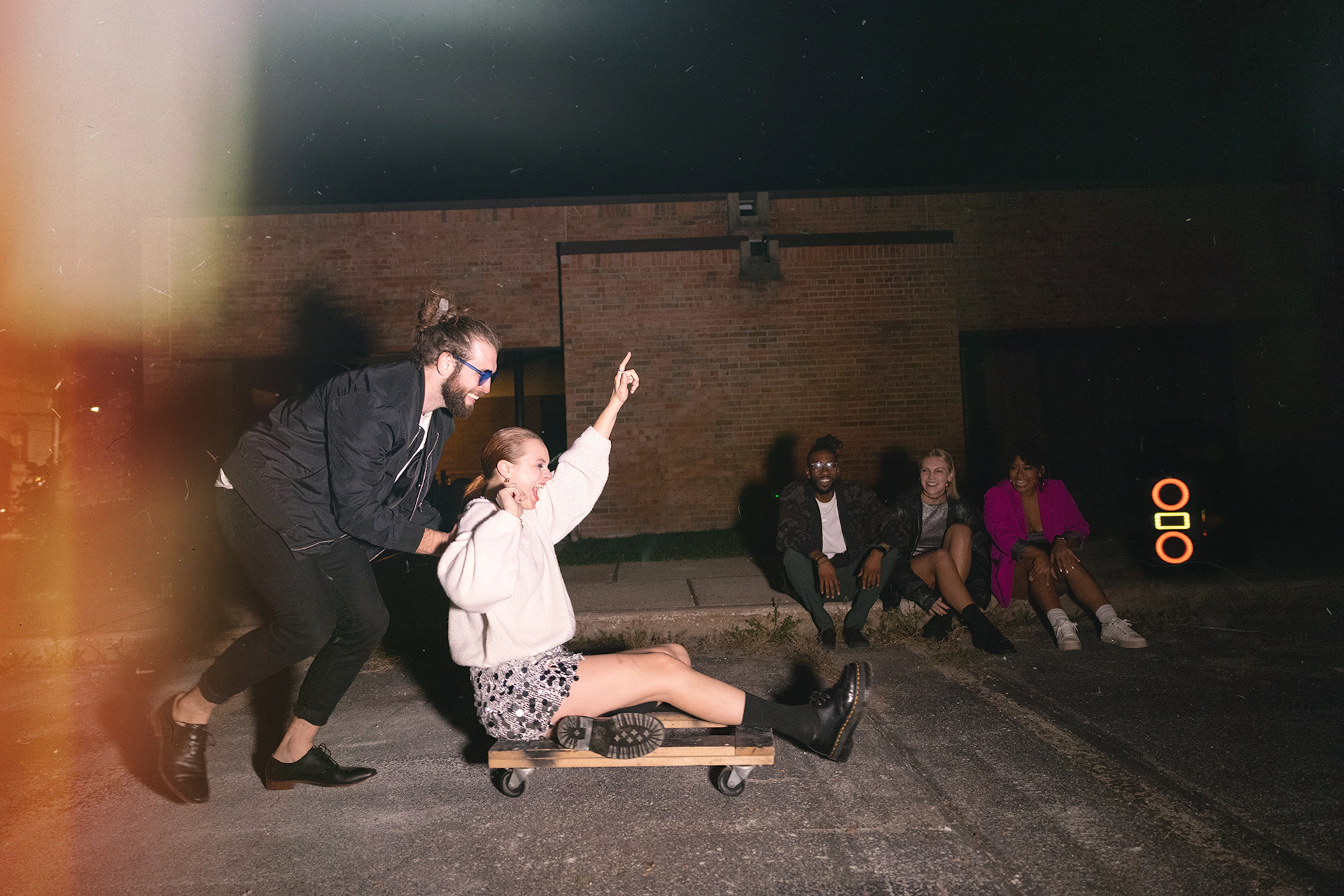 Хлопець із Klipsch Party Speakers Vibe штовхає жінку на меблевому візку на парковці 2000x1333