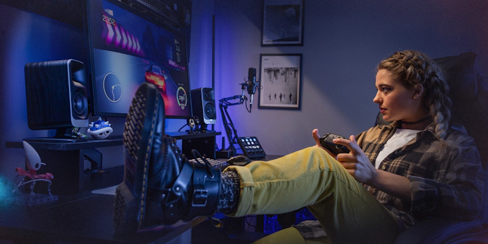 Klipsch Pro Media Lumina Computer Speakers on gamer desk setup with female gamer playing racing game with foot on desk 2000x1000