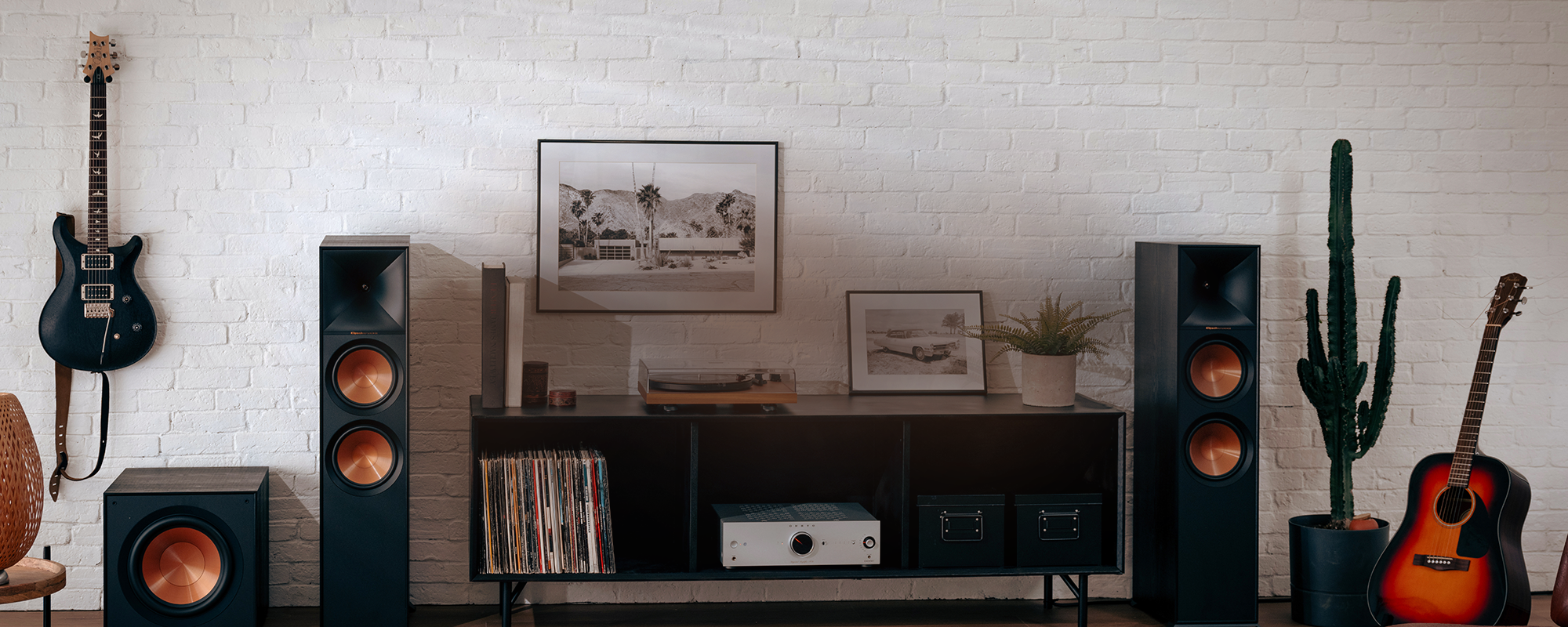 Klipsch Reference system with Onkyo amplifier and record player against white brick wall beside cactus and guitar 2000x800