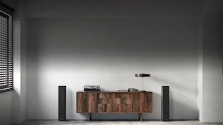 Колонки RP 5000 F расположены по бокам красивой деревянной комоды с настольной лампой и книгами на ней