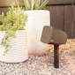 Klipsch Courtyard Speaker outdoors in gravel beside stylish white planters 2000x2000
